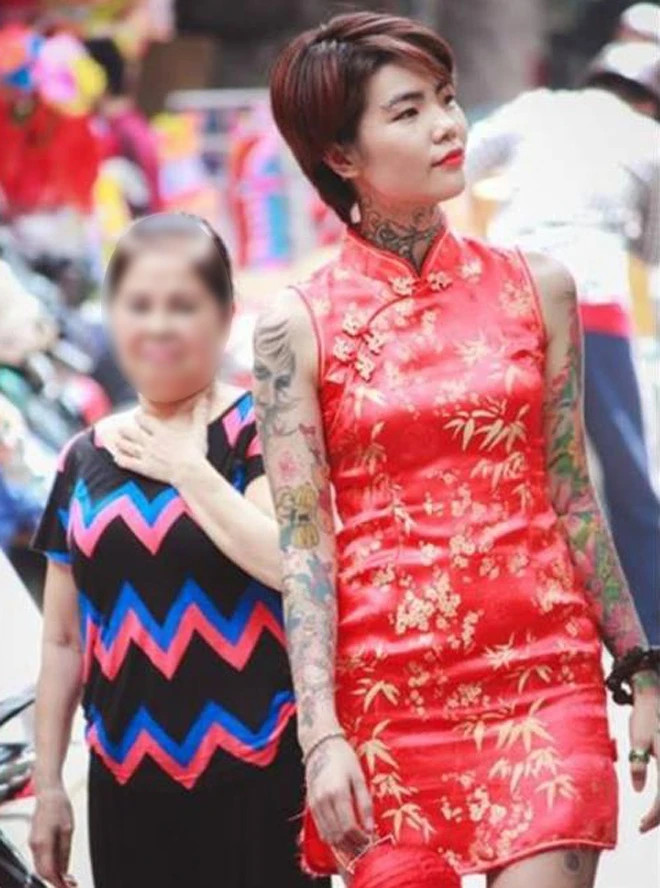 Cô gái xăm trổ Phạm Huỳnh Mai trong tà áo dài đỏ nổi bật trên phố, phía sau là ánh nhìn không mấy thiện cảm của một phụ nữ lớn tuổi