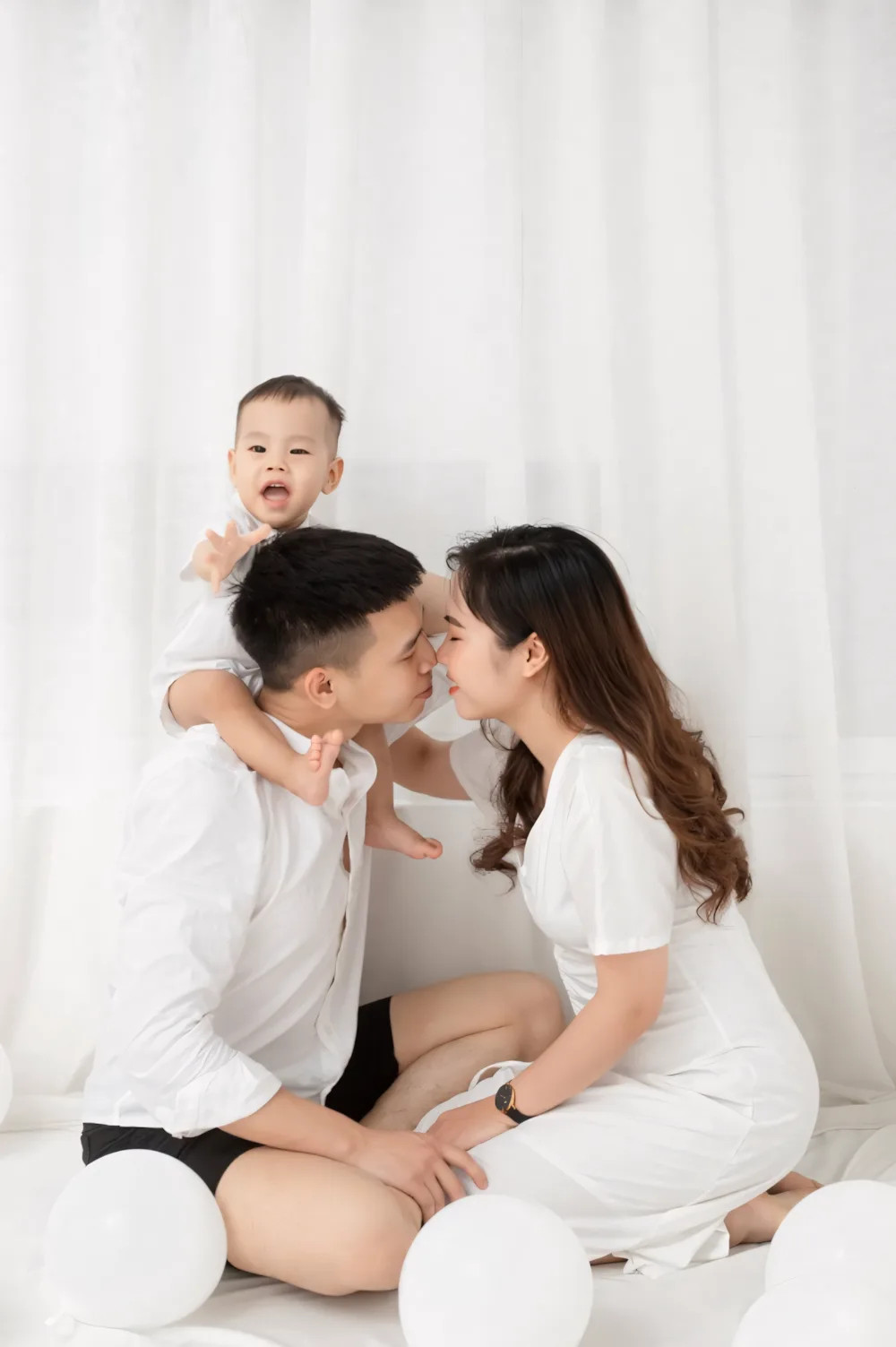 Gia đình ba người mặc trang phục tông trắng tại phim trường chụp ảnh